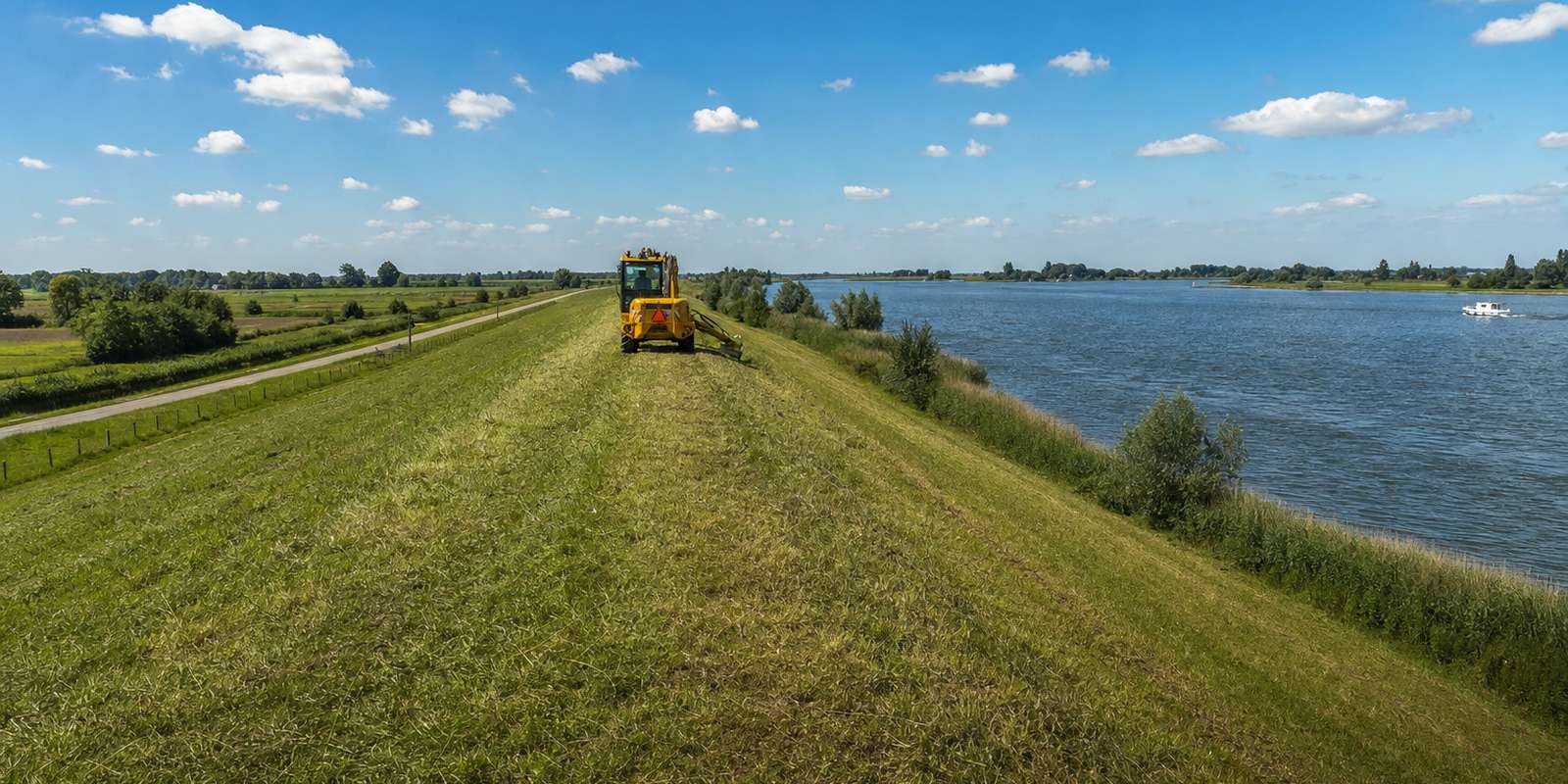 Met gras begroeide dijk langs een brede rivier
